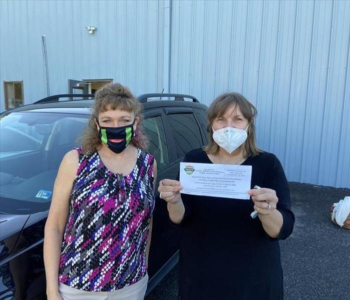 Radio-game winner holding up her certificate for a car disinfecting, next to SERVPRO of Charlottesville Marketing Manager.