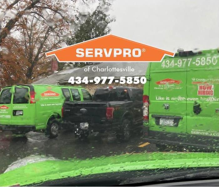 Several SERVPRO of Charlottesville vehicles are shown responding to a water damage emergency on a rainy day. 