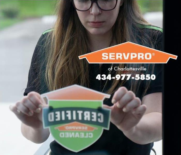 A SERVPRO of Charlottesville technician is placing a Certified: SERVPRO Cleaned sticker on the door to a commercial property 
