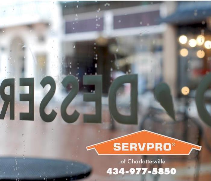 A view of a rainy day is shown through the store front window of a bakery. 
